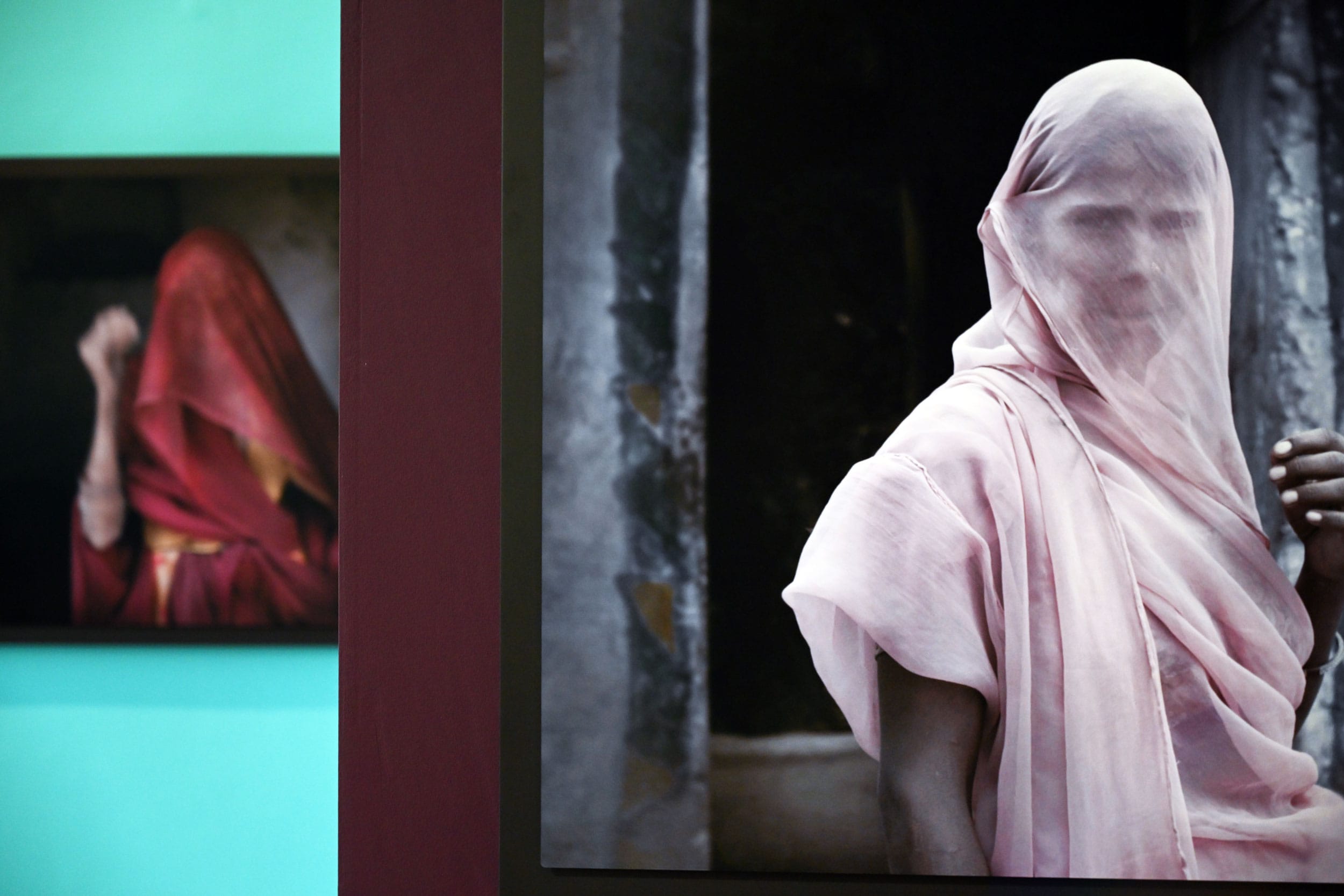 Photographs of people in veils displayed on a wall in an art exhibition setting.