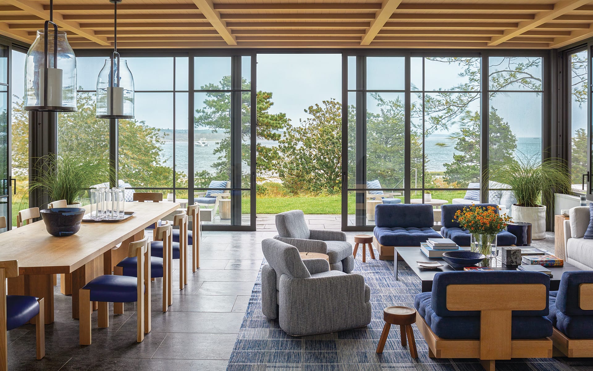 Modern open-concept living and dining area with large windows overlooking a scenic ocean view, featuring stylish furniture and decor.