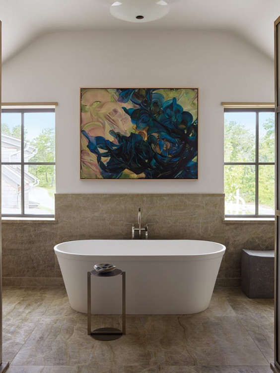 Modern bathroom with a freestanding tub, abstract artwork, and large windows providing natural light and outdoor views.