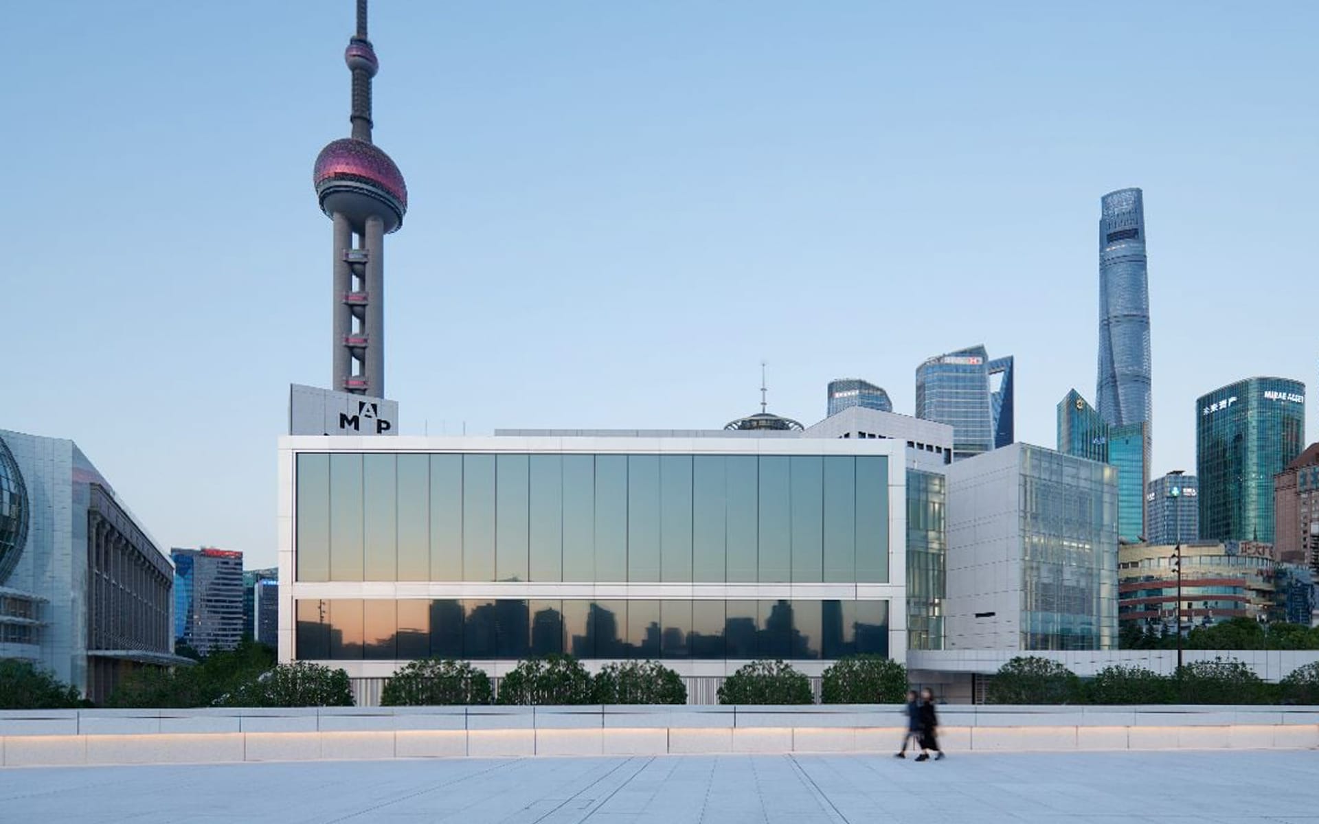 Modern building with glass facade reflecting Shanghai skyline, including the Oriental Pearl Tower, during sunset.