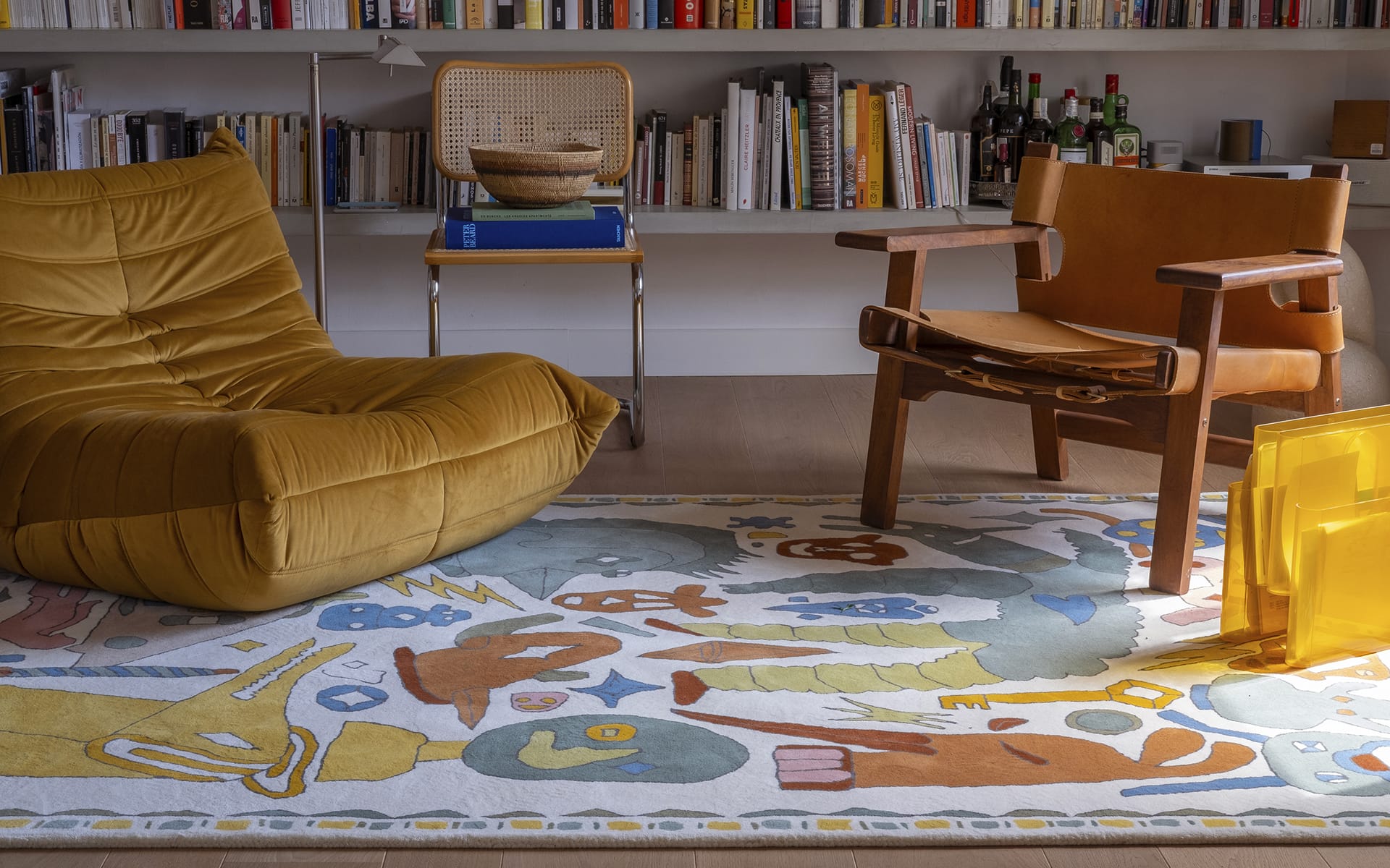 Cozy living room with yellow bean bag, wooden chair, colorful rug, and bookshelves in the background.