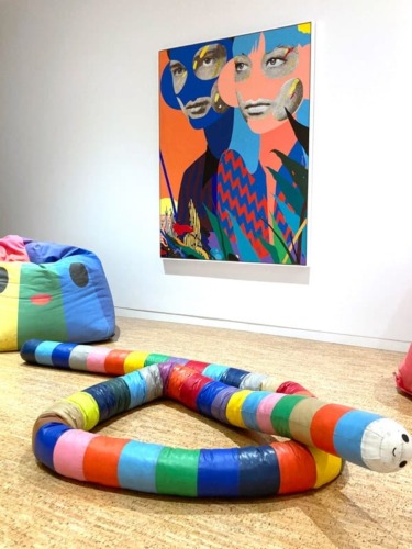 Colorful abstract art displayed in a gallery with a vibrant snake-like sculpture on the floor.