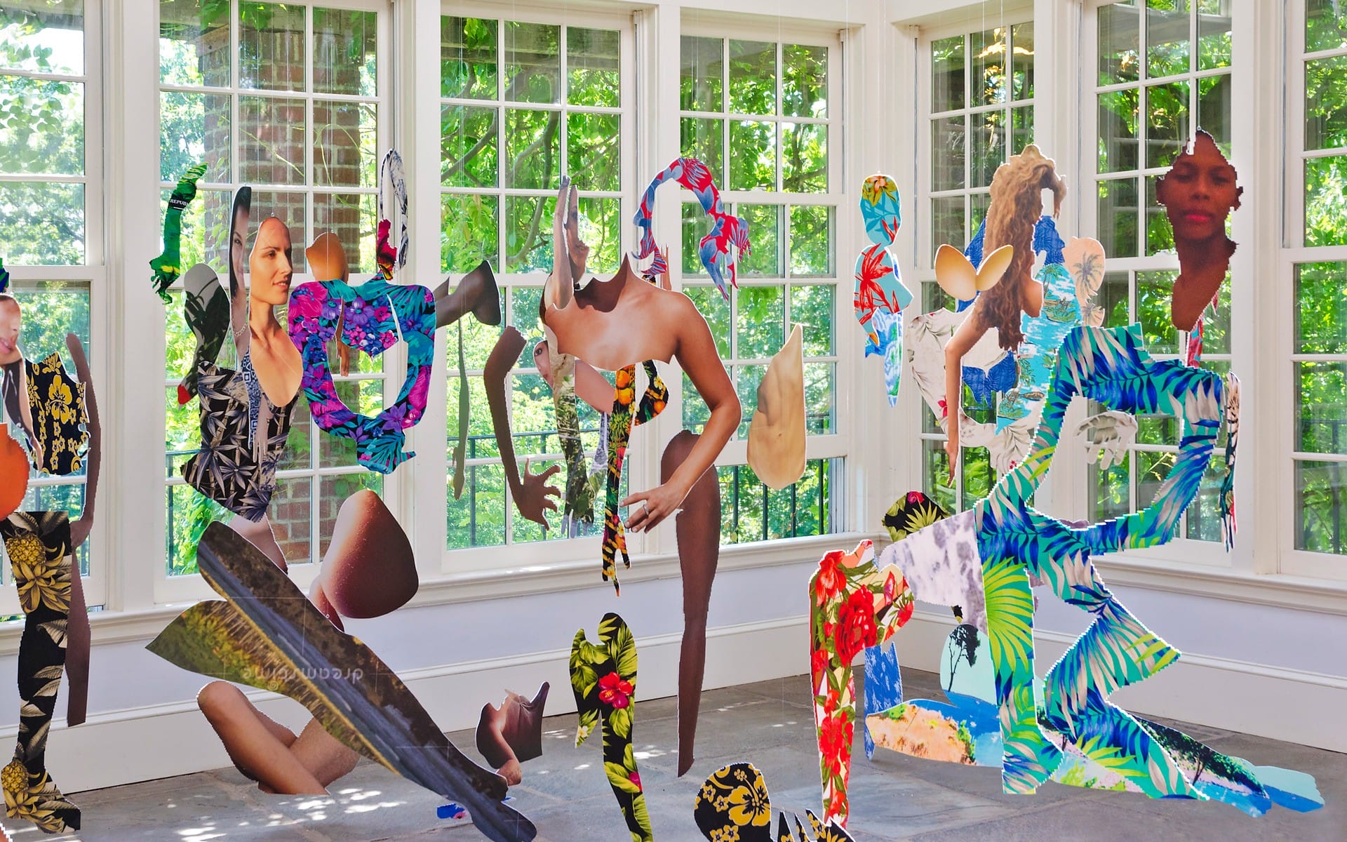 Colorful abstract collage of cut-out figures in a sunlit room with large windows and greenery outside.