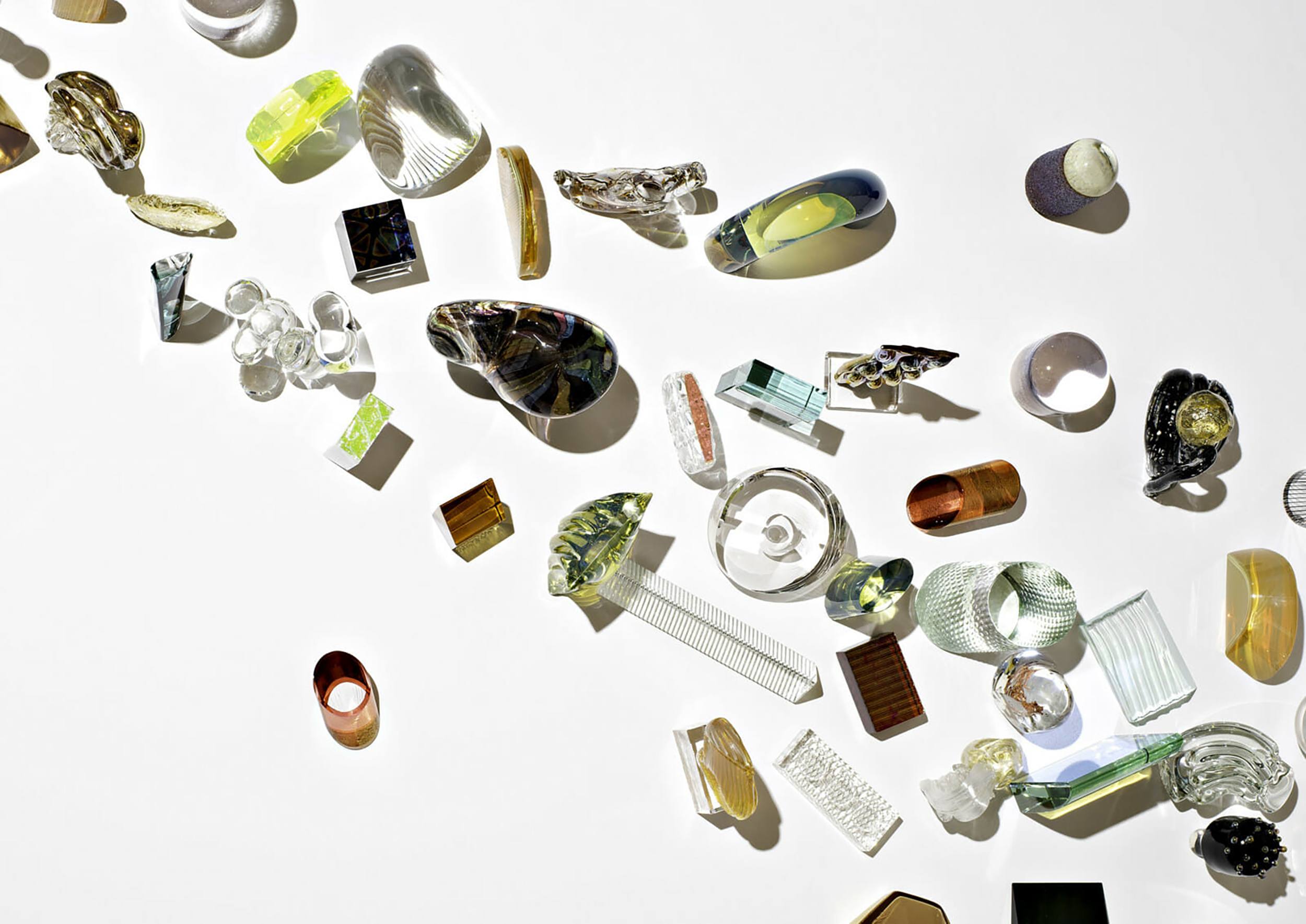 Assorted transparent and colorful glass shapes scattered on a white surface.