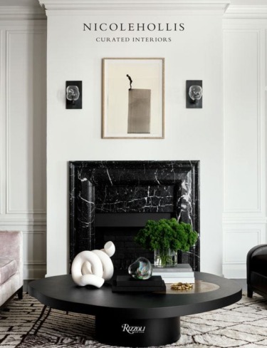 Modern living room with black marble fireplace, art, and sleek round coffee table with decor and greenery.