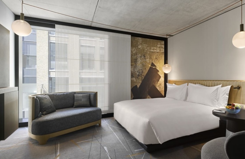 Modern hotel room with a large bed, stylish artwork, a sofa, and large windows providing natural light.