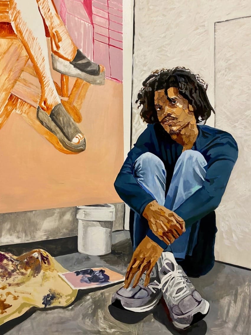 Person seated on floor, leaning against wall, with painting supplies nearby, and artwork in progress on the wall.