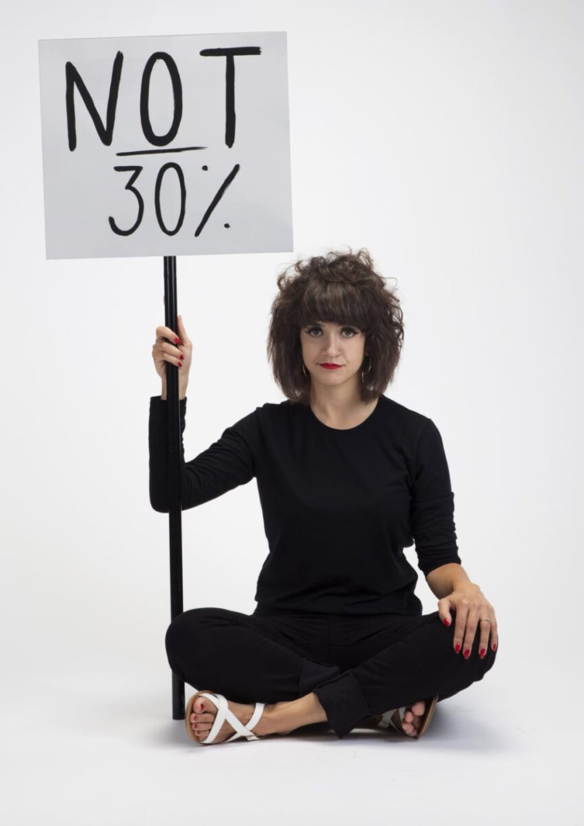 Person sitting cross-legged holding a sign that reads "NOT 30%" against a plain white background.
