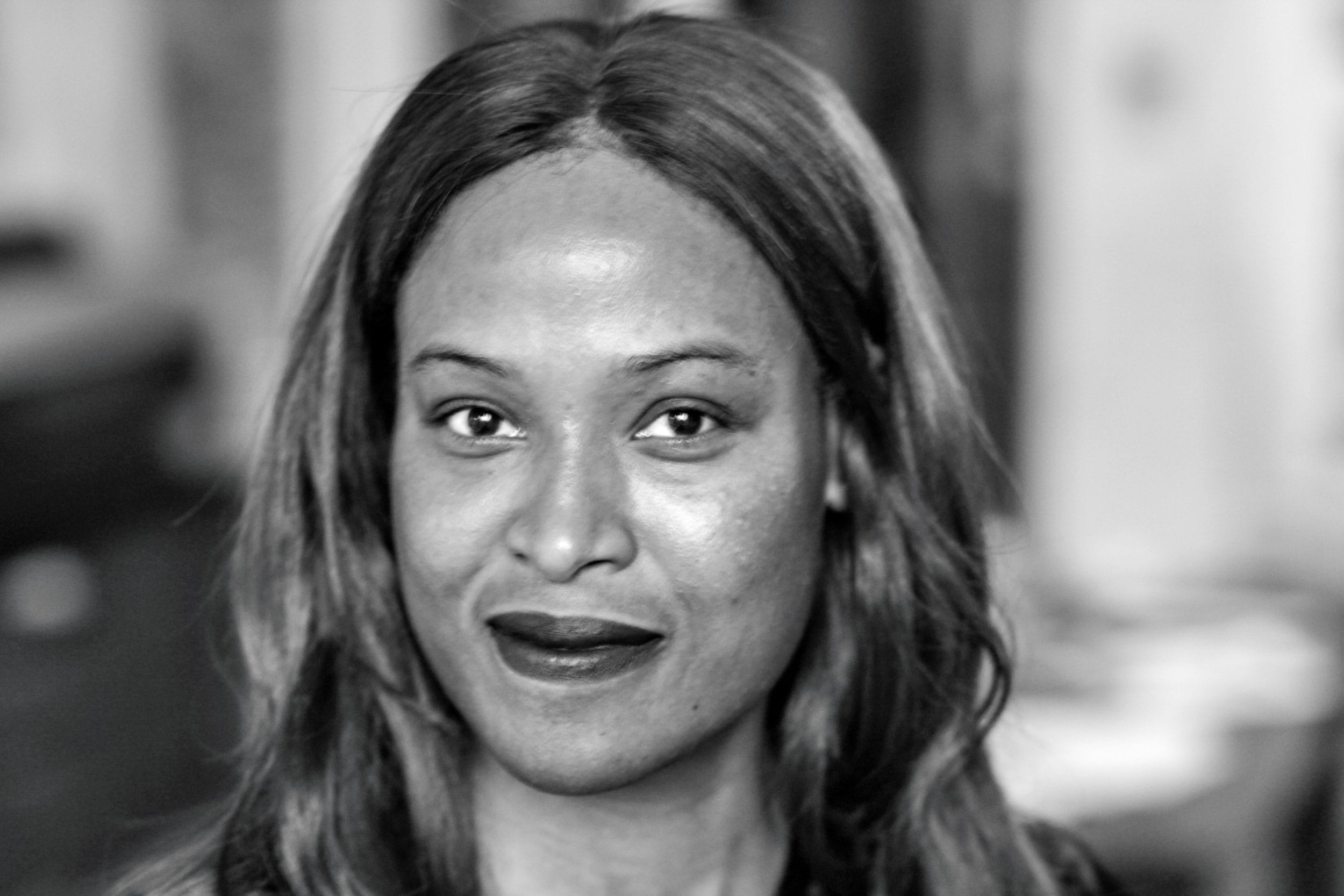 Black and white portrait of a person with long hair smiling softly, set against a blurred background.
