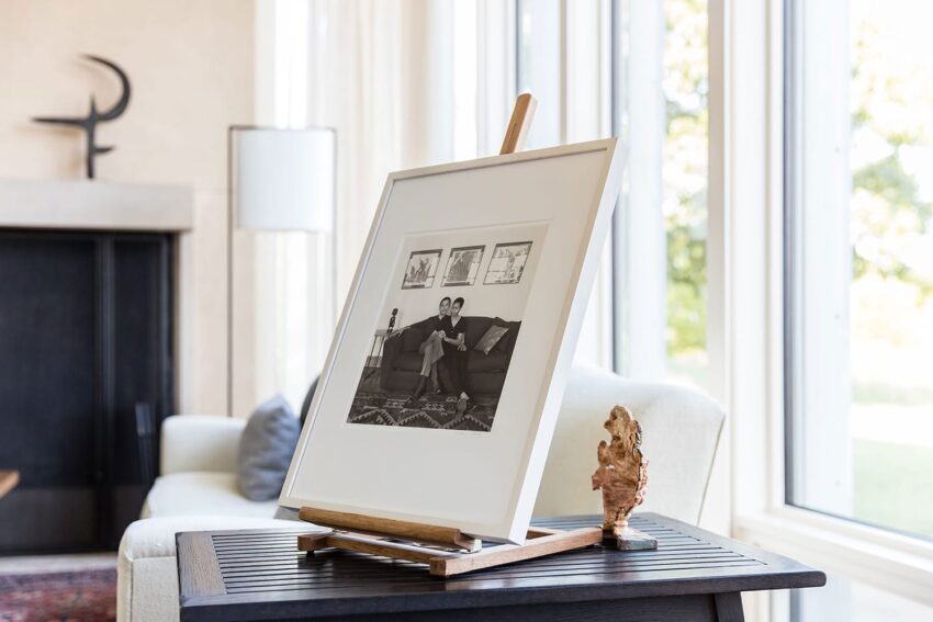 Easel displaying a framed black and white photo on a table, with a modern living room in the background.