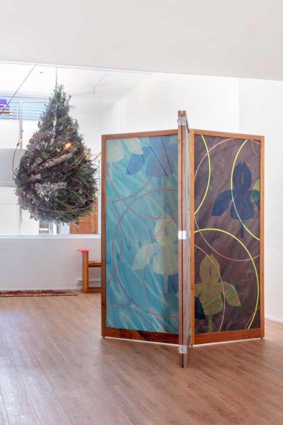 Artistic room divider with floral patterns next to a suspended Christmas tree in a modern, minimalist interior setting.
