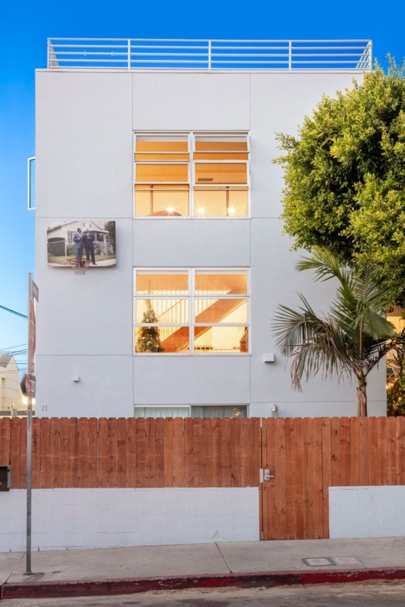 Modern white three-story building with large windows, wooden fence, and a basketball hoop on a sunny day.