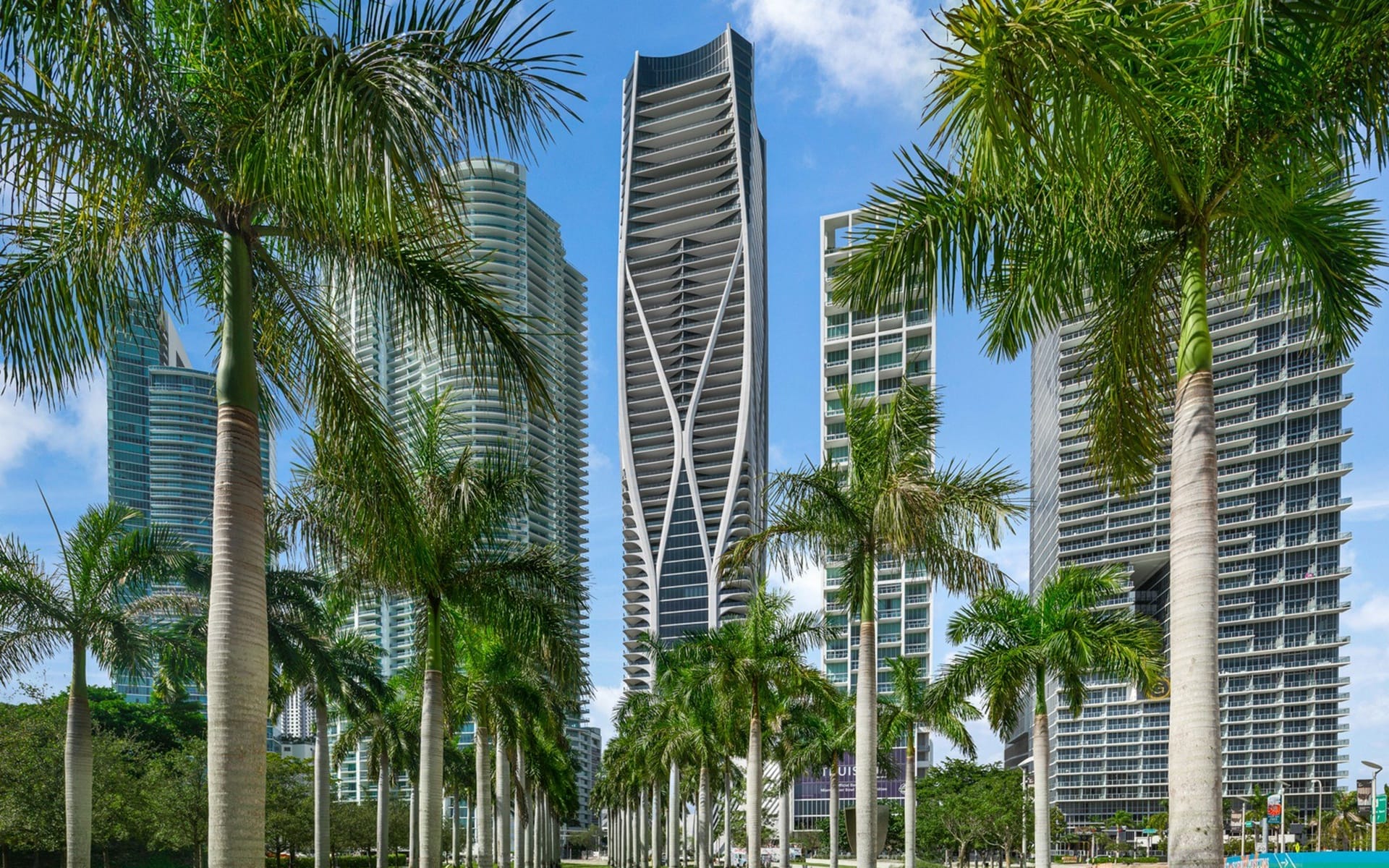 Modern skyscrapers with unique architecture surrounded by tall palm trees under a clear blue sky.