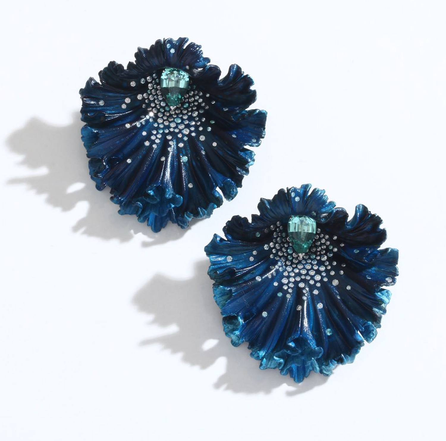 Blue statement floral earrings with shimmering silver accents and a central green gem on a light background.