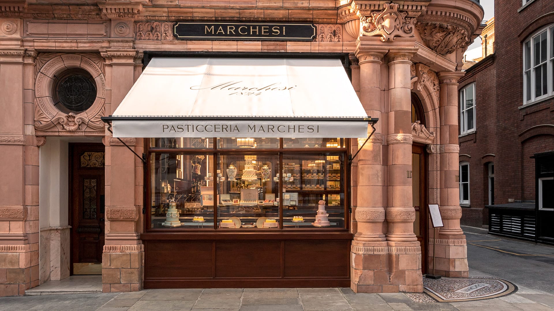 Exterior of a vintage bakery with ornate architecture and an awning displaying "Pasticceria Marchesi" above a window of pastries.
