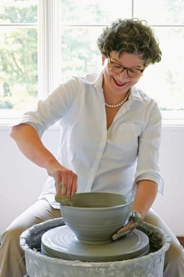 Woman smiling while shaping clay on a pottery wheel in a bright room.