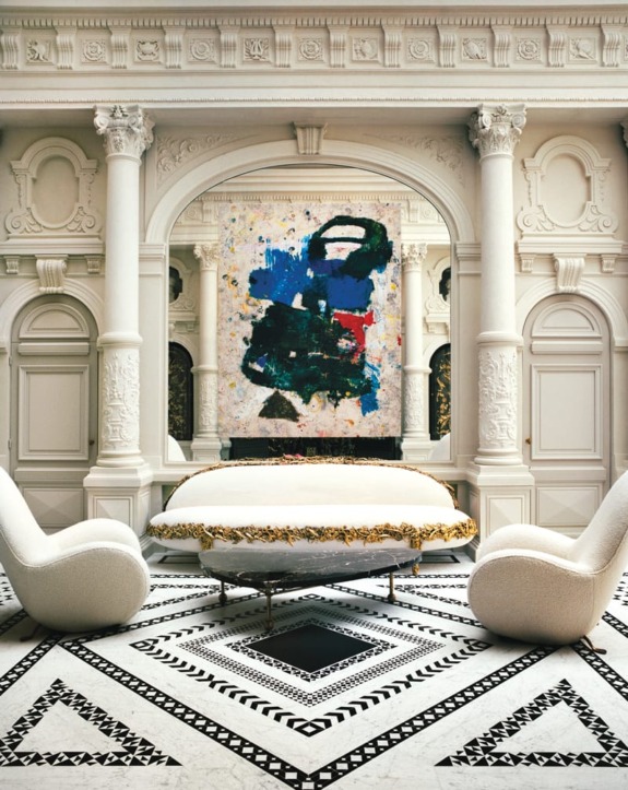 Elegant room with ornate architecture, featuring a large abstract painting, white couch, and two modern chairs.