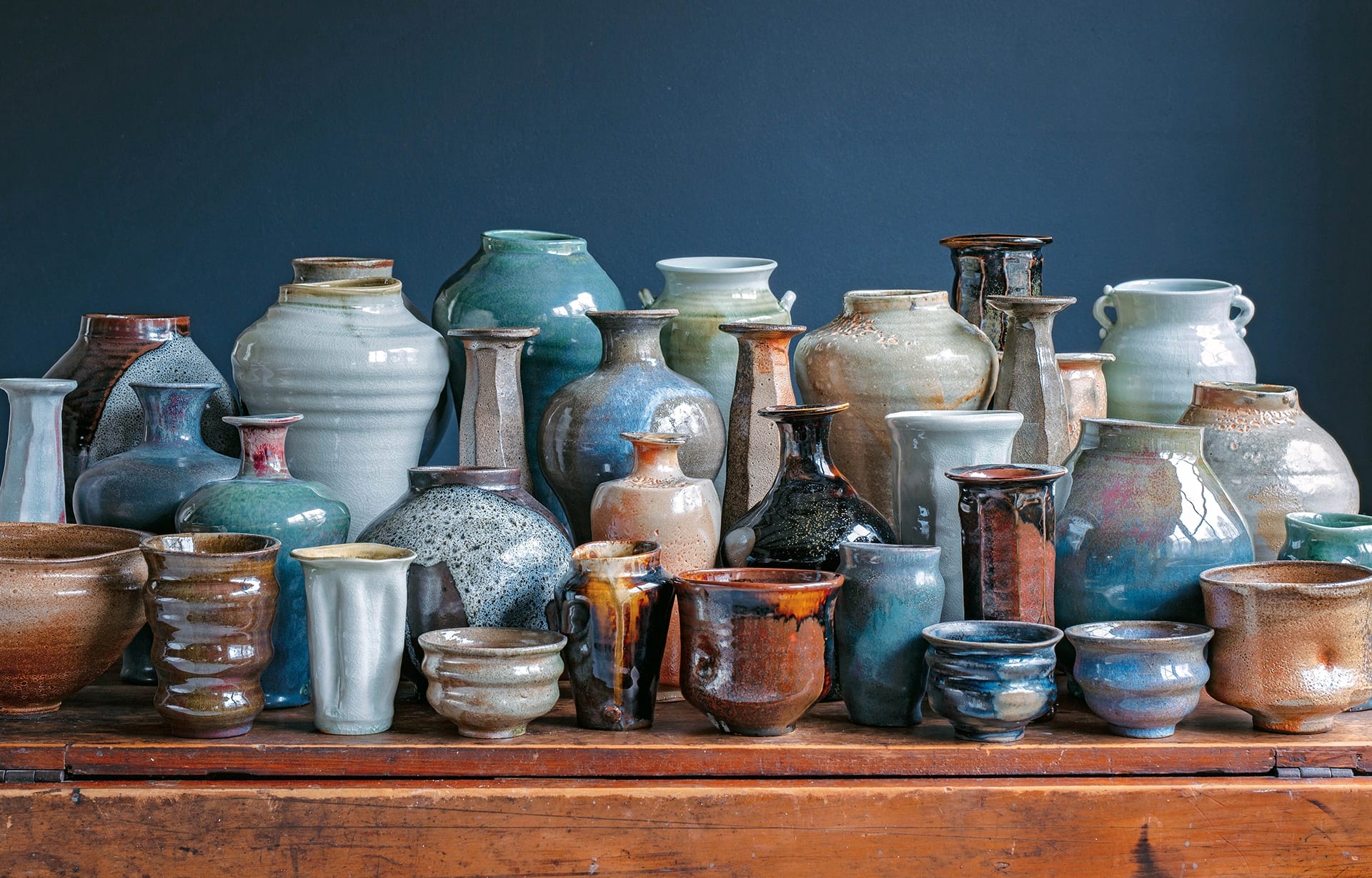 A collection of various ceramic pots and vases displayed on a wooden surface against a dark background.