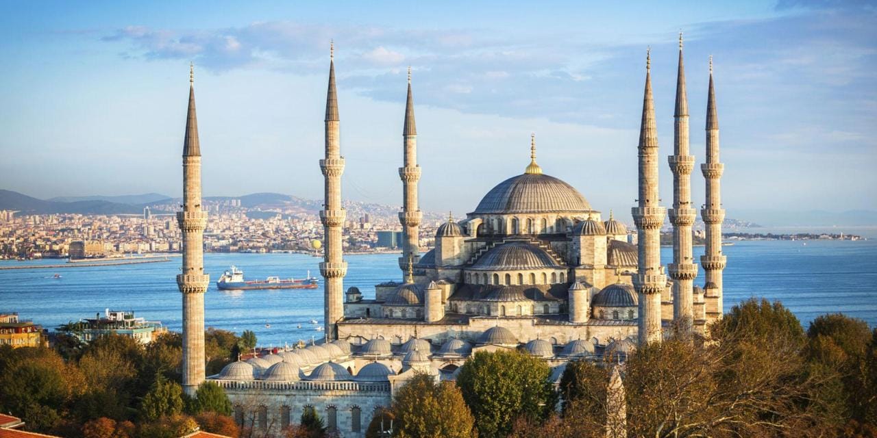 Blue Mosque in Istanbul with six minarets, overlooking the Bosphorus, surrounded by trees and cityscape in the background.