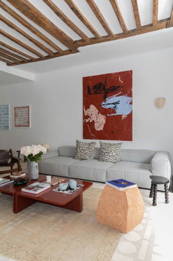 Modern living room with gray sofa, abstract painting, wooden beams, decorative pillows, and a red coffee table.