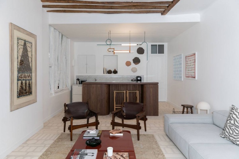 Modern living room with wooden beams, stylish furniture, abstract art, and a minimalist kitchen in the background.