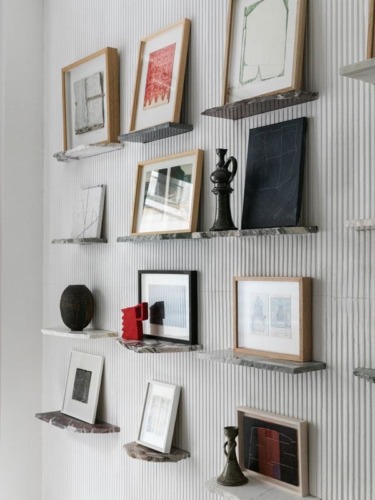 Wall-mounted shelves displaying various framed artworks and decorative objects in a modern interior setting.