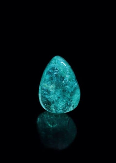 Teardrop-shaped blue gemstone with a reflective surface on a black background