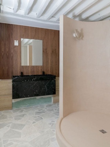 Modern bathroom with black marble sink, wooden backsplash, and round beige shower area on patterned flooring.