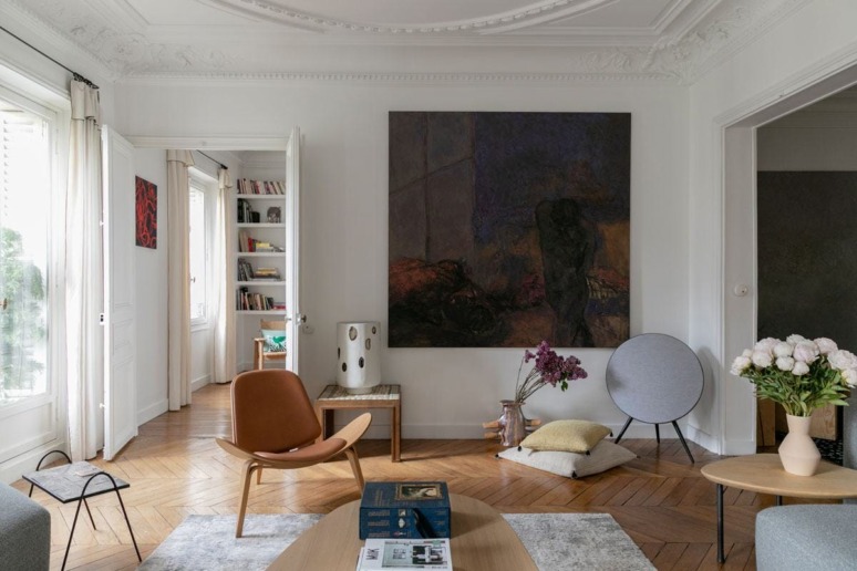 Elegant living room with modern decor, large abstract painting, wooden flooring, and a mix of minimalist furniture.