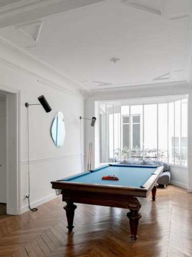 Billiard room with a pool table, wooden floor, modern wall lighting, and a large window offering natural light.