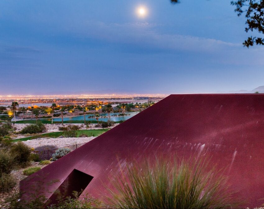 Cityscape view at dusk with a red building in the foreground, a full moon in the sky, and a distant city illuminated below.