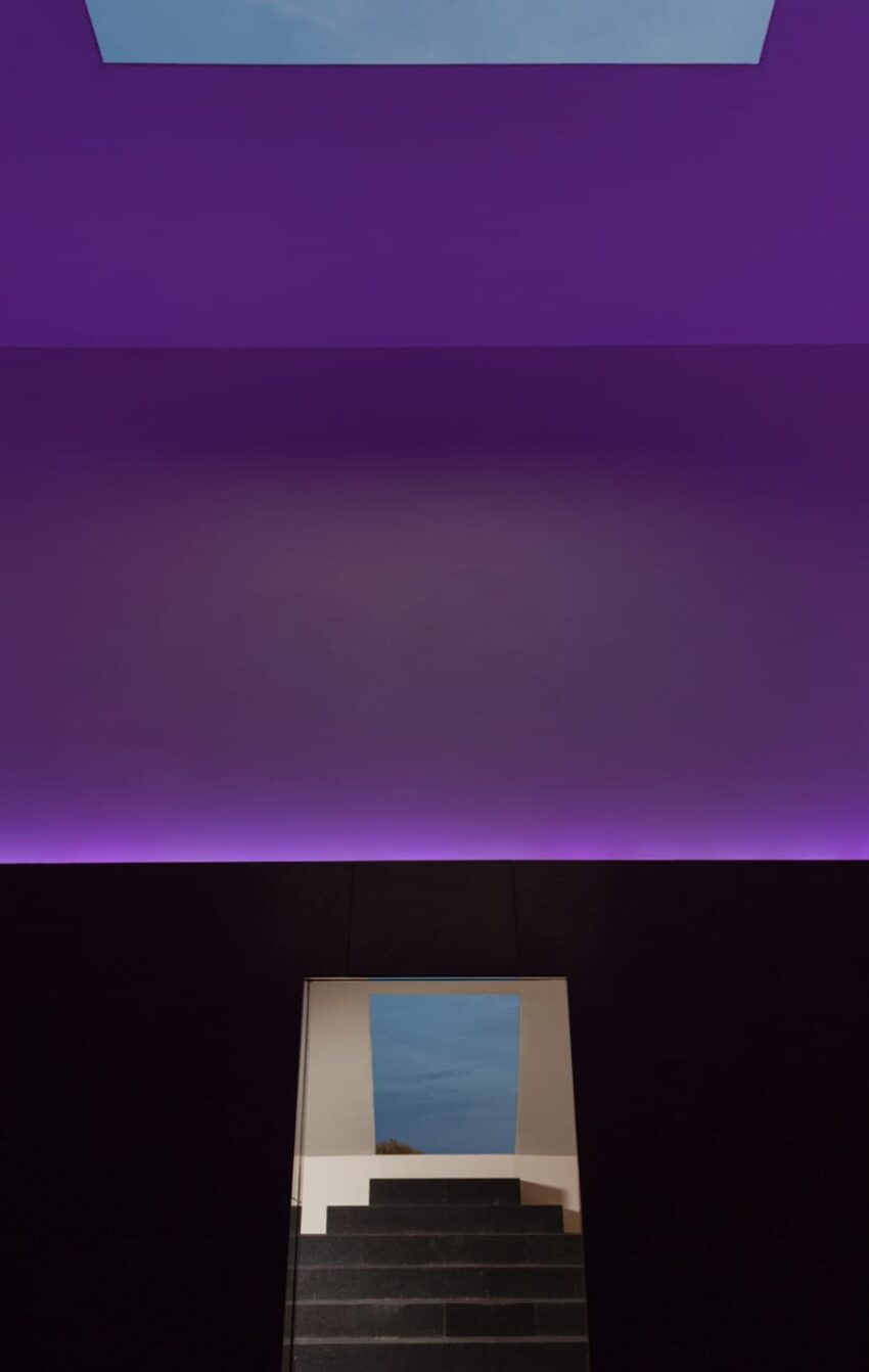 Modern interior with purple-lit ceiling, dark staircase, and a square skylight showing a patch of blue sky.