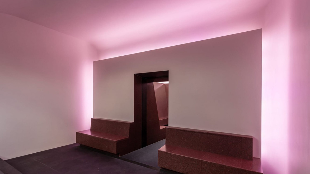 Modern interior with pink ambient lighting, featuring two bench seats flanking a dark entrance in a minimalist design.
