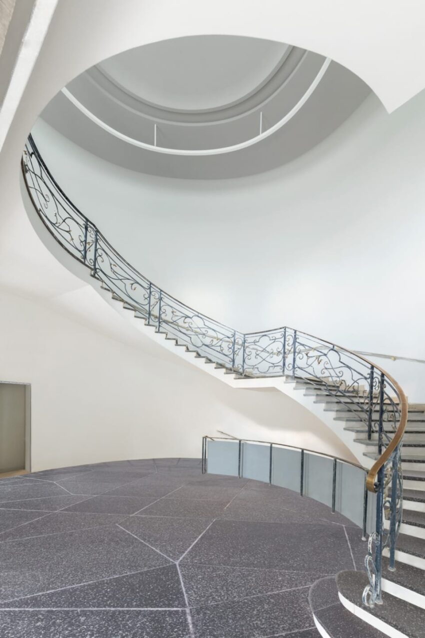 Elegant spiral staircase with ornate iron railing in a modern interior, featuring a circular design and polished stone floor.