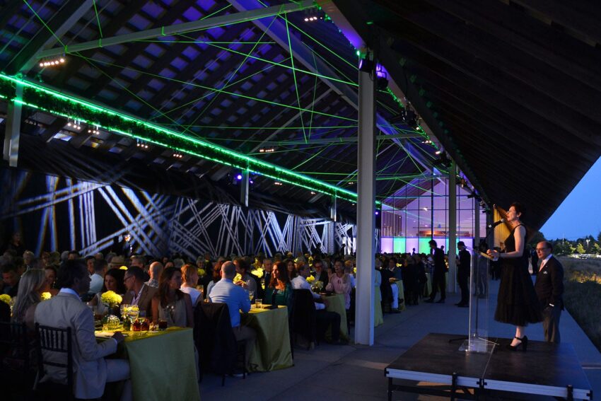 Evening event in a modern, illuminated venue with a speaker on stage and seated audience.