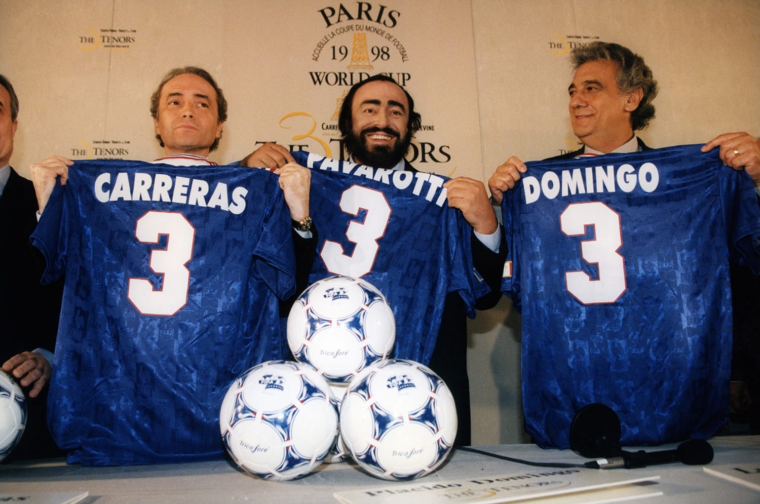 Three men hold blue soccer jerseys with the number 3 displayed, set against a backdrop with World Cup branding.