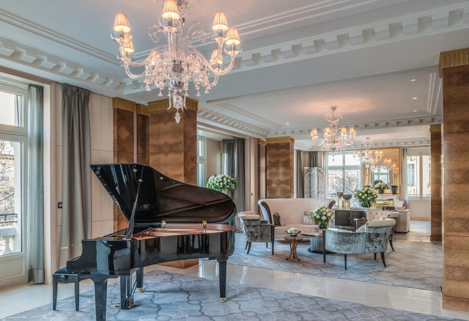 Luxurious hotel suite with a grand piano, elegant chandeliers, and plush seating near large windows.