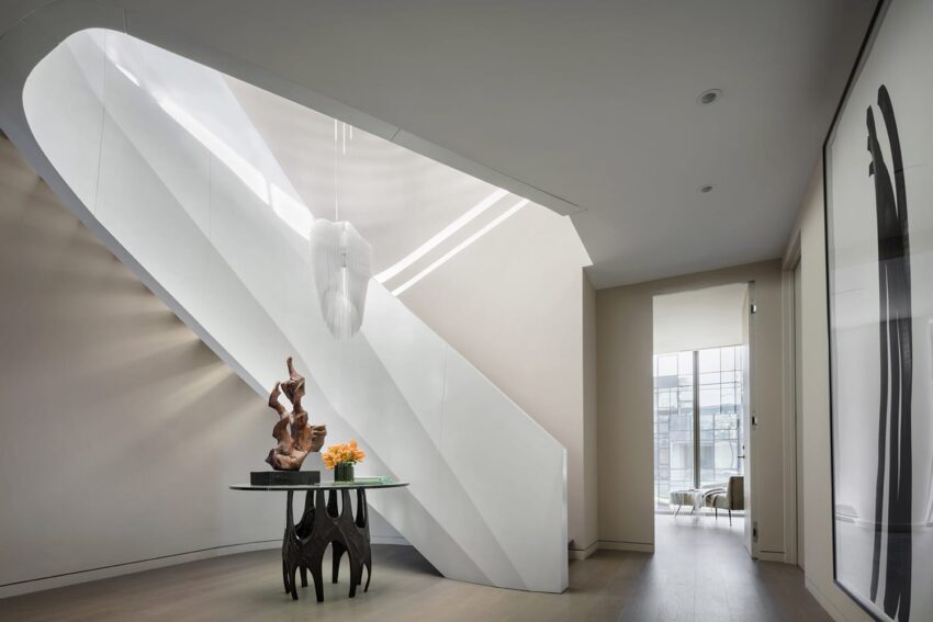 Modern interior with minimalist staircase, sculpture on glass table, and sunlight streaming from window.
