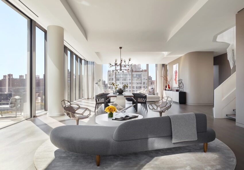 Modern living room with large windows, elegant gray furniture, round coffee table, and cityscape view.