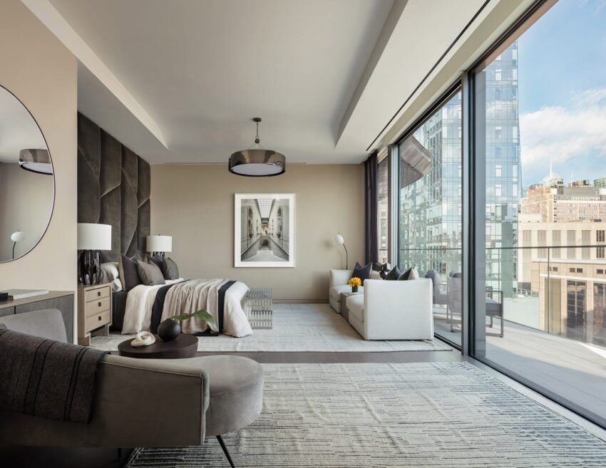Modern bedroom with large windows, city view, stylish furniture, cozy bed, patterned rug, and contemporary artwork.