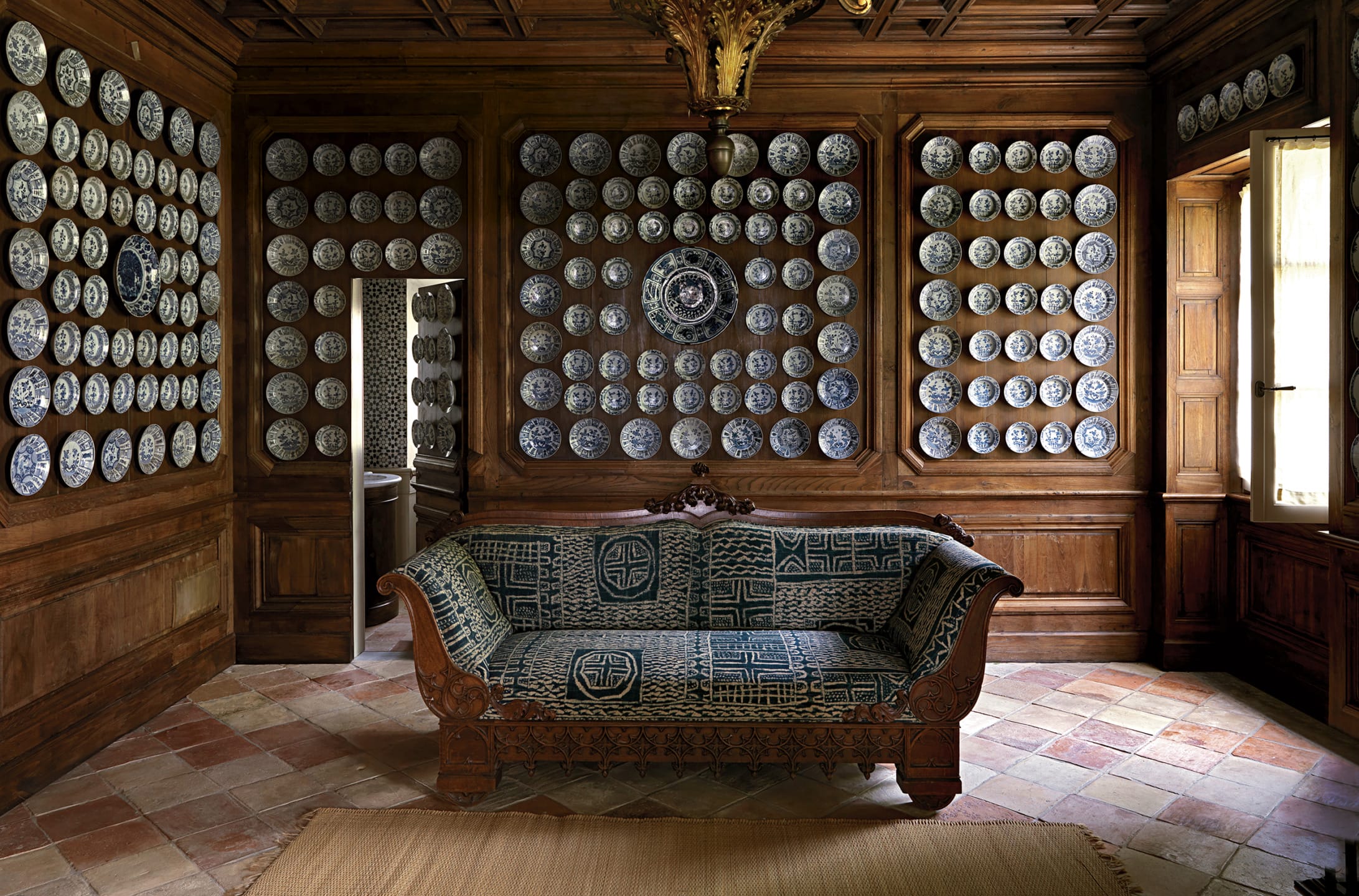 Room with wood paneling features a decorative couch and walls adorned with multiple blue and white ceramic plates.