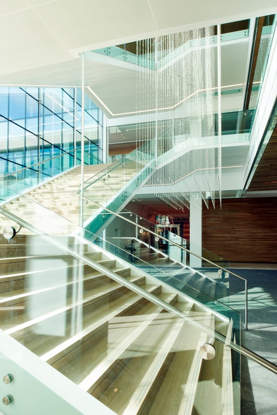 Modern office building interior with glass staircases, large windows, and elegant lighting fixtures.