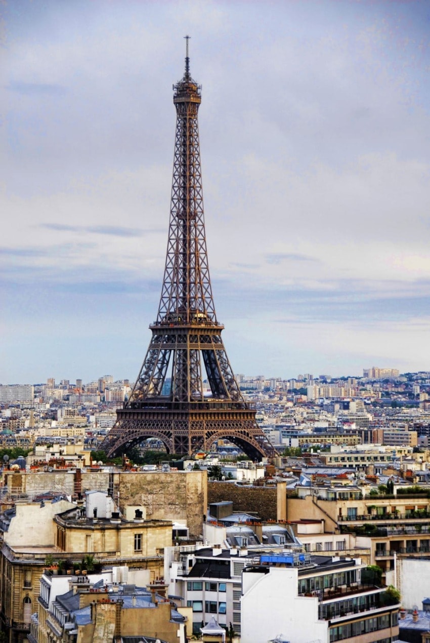 Eiffel Tower standing tall in Paris skyline with city buildings and cloudy sky in the background.