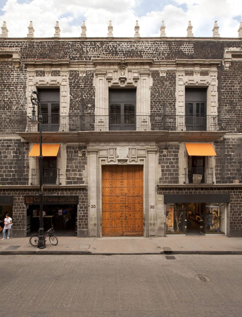 Historic colonial building with a large wooden door, two balconies, and a cobblestone facade on a quiet street.