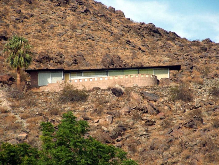 Modern house built into arid hillside with sparse vegetation and a lone palm tree nearby.