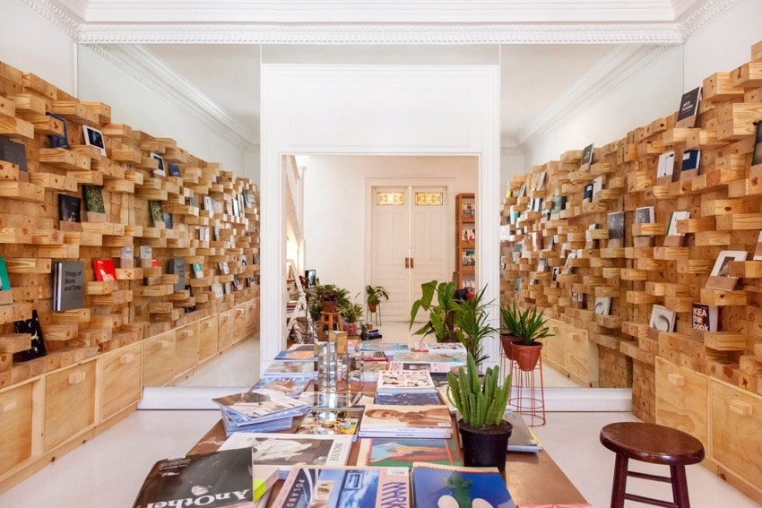 Modern interior with magazine display, wooden shelves filled with books, and plants on a central table.