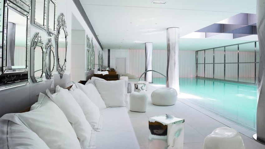 Modern indoor swimming pool with white seating area, mirrors on the wall, and sleek design elements.