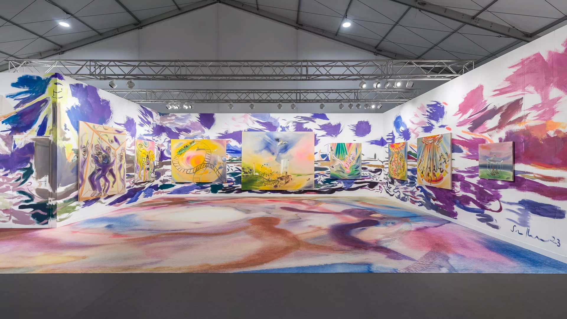 Art exhibit with colorful abstract paintings and vibrant patterns on walls and floor in a spacious gallery setting.