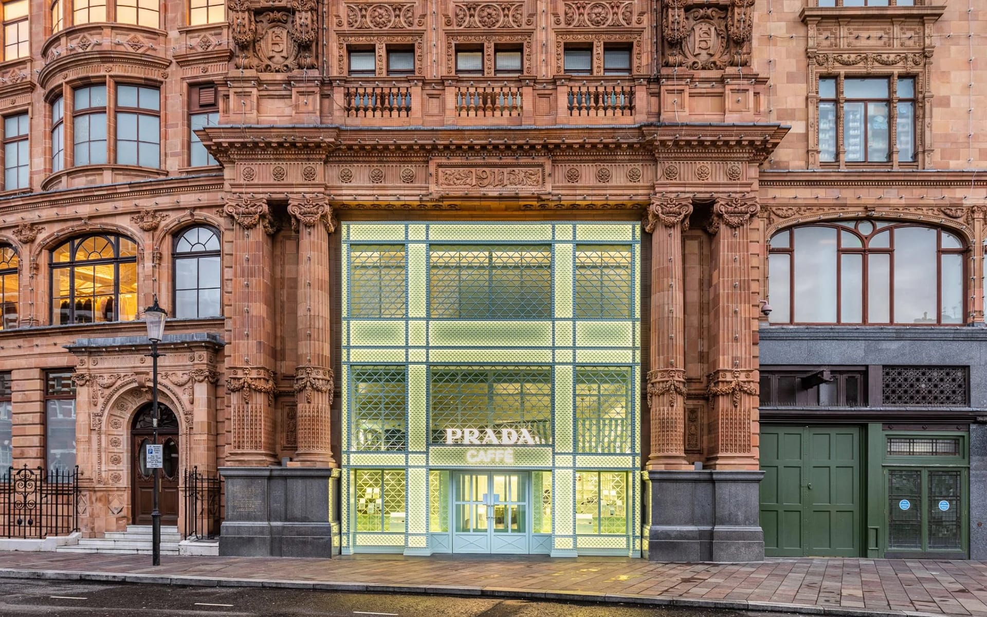 Exterior view of Prada Caffè with ornate architectural details and illuminated entrance on a city street.