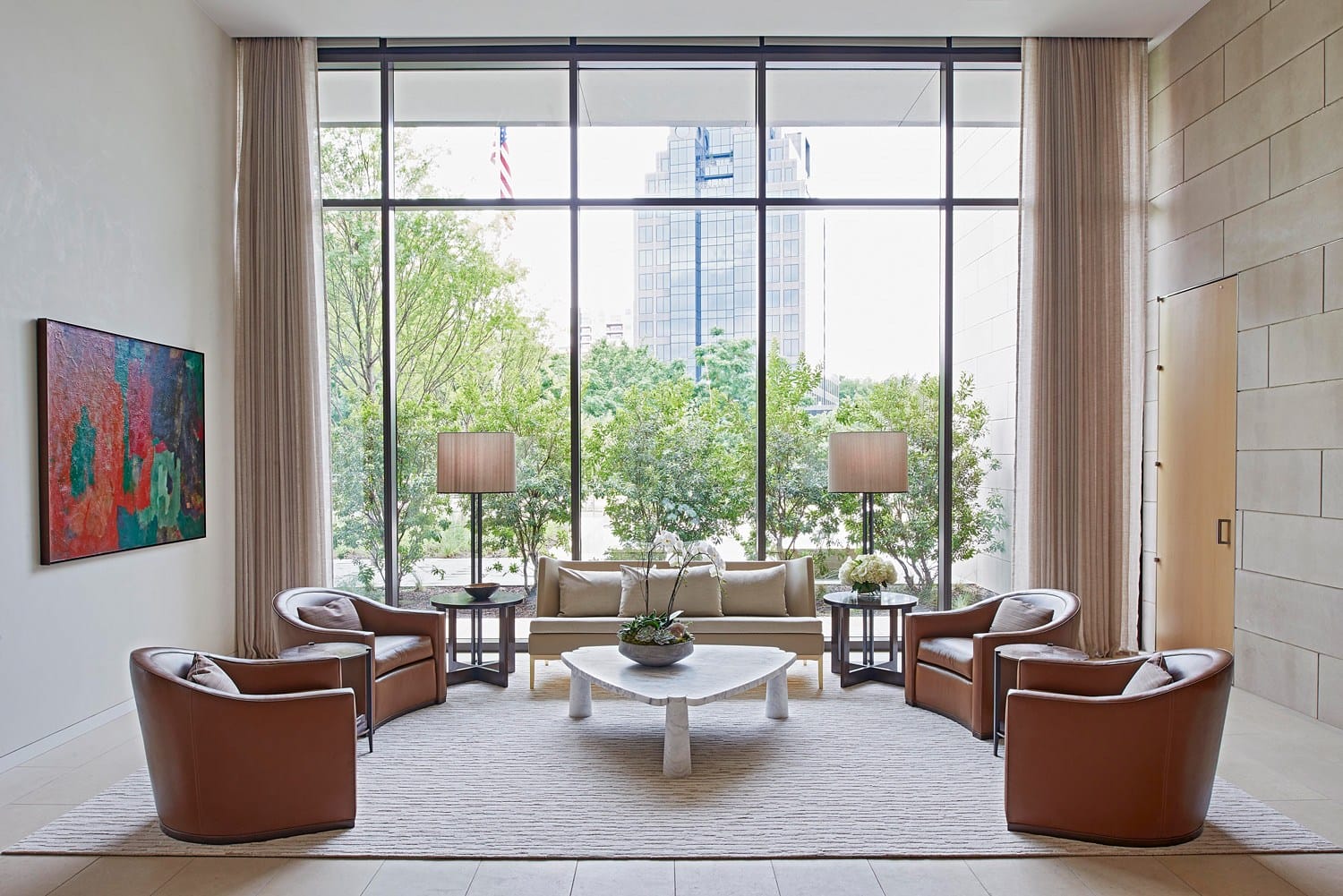 Modern living room with large windows, brown leather chairs, a white coffee table, and a cityscape view in the background.